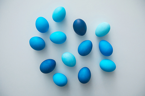 Above view of hand-painted blue Easter eggs arranged in minimal composition on white background, copy space