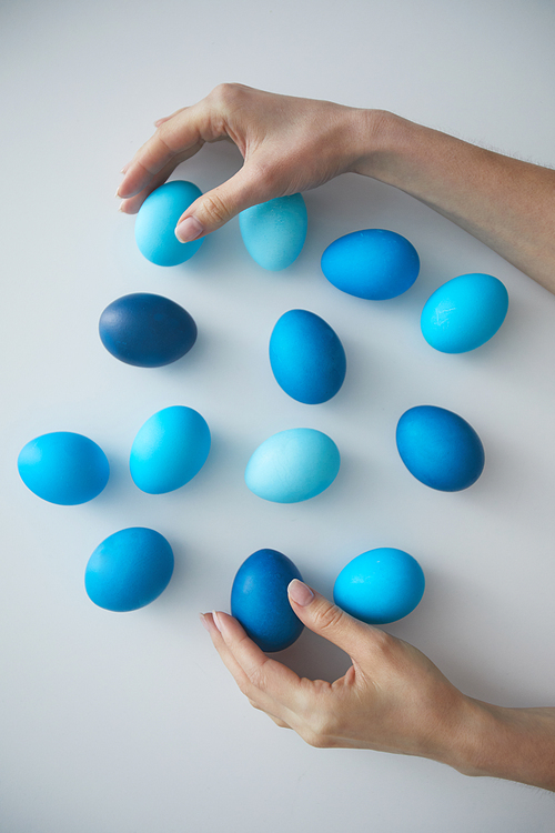Above view background female hand arranging composition of painted blue Easter eggs on white, copy space