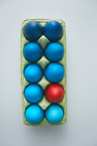 Above view of blue Easter eggs in crate with red accent arranged in minimal composition on white background, copy space