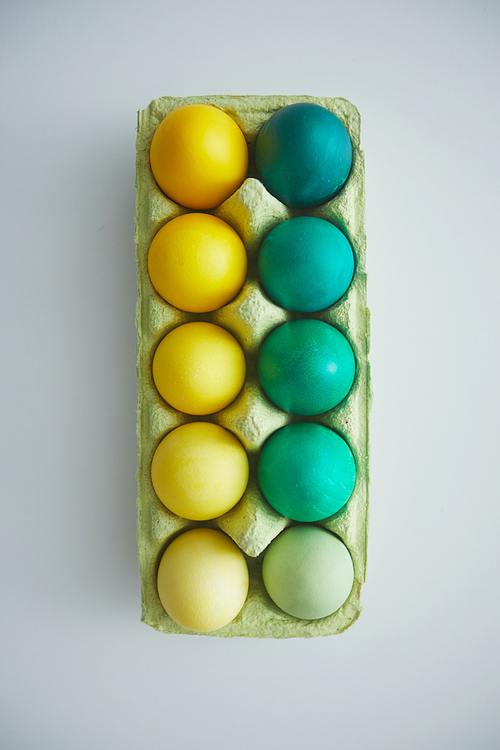 Above view of green and yellow hand painted Easter eggs in crate arranged in minimal composition on white background, copy space