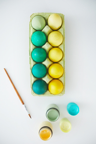 Above view of green and yellow hand painted Easter eggs in crate arranged in minimal composition with paint brush on white background, copy space