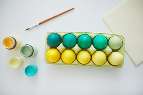 Top view of green and yellow hand painted Easter eggs in crate arranged in minimal composition with paint brush on white background, copy space