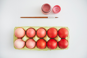 Top view of pastel pink and red Easter eggs in crate arranged in minimal composition with paint brush on white background, copy space