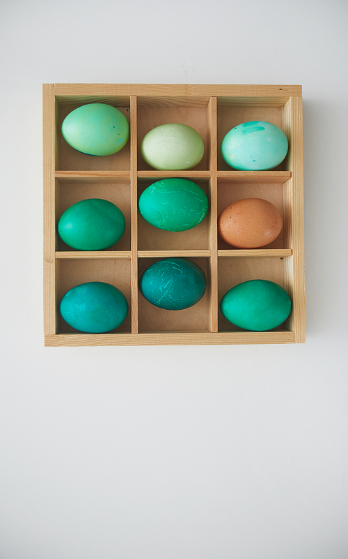 Top view of hand-painted emerald Easter eggs in wooden crate arranged in minimal composition on white background, copy space