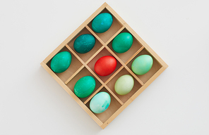 Top view of green Easter eggs with red accent in wooden crate, minimal composition on white background, copy space