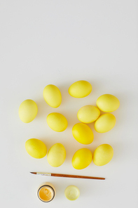 Top view of pastel yellow Easter eggs with paint brush arraigned in minimal composition on white background, copy space