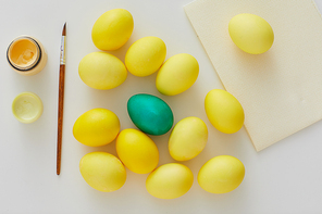 Above view of pastel yellow Easter eggs with green accent and paint brush arraigned in minimal composition on white background, copy space