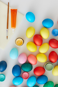 Above view of multi colored Easter eggs with paint brushes arraigned in minimal composition on white background in art studio, copy space
