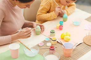 High angle portrait of mother and daughter painting Easter eggs pastel colors sitting at table in cozy kitchen interior, copy space