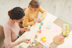 High angle view at mother and daughter painting Easter eggs pastel colors sitting at table in cozy kitchen interior, copy space