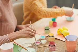 Closeup of unrecognizable mother and daughter painting Easter eggs pastel colors sitting at table in cozy kitchen interior, copy space