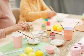 Close up of unrecognizable mother and daughter painting Easter eggs pastel colors sitting at table in cozy kitchen interior, copy space
