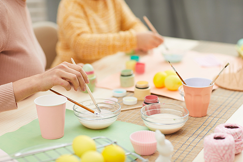Close up of unrecognizable mother and daughter painting Easter eggs pastel colors sitting at table in cozy kitchen interior, copy space