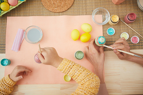 Top view close up mother and daughter painting Easter eggs pastel colors sitting at table in kitchen interior, copy space