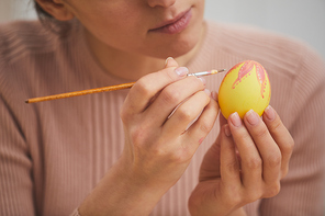 Close up of elegant young woman painting intricate design on Easter egg, copy space