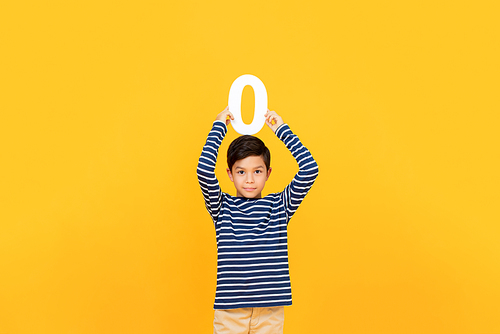 10 year-old cute little boy holding number zero overhead on yellow background