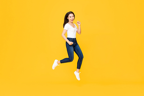 Full length portrait of pretty Asian woman smiling and jumping in mid-air isolated on yellow background