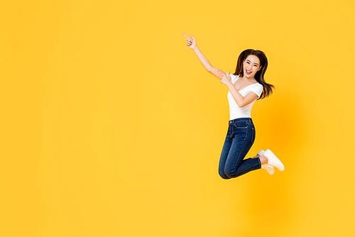 Happy smiling young Asian girl jumping with hands poiting up isolated on yellow studio background with copy space