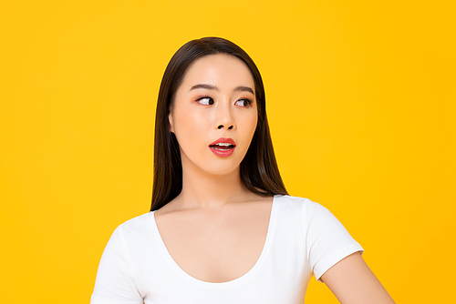 Close-up portrait of a curious young Asian woman thinking while anxiously looking at the side in isolated studio yellow background