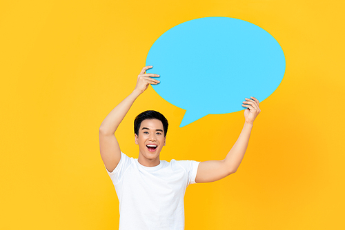 Happy smiling young handsome Asian man holding speech bubble with empty space for text on colorful yellow background