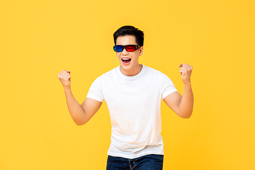 Waist up portrait of ecstatic young Asian man wearing 3D movie glasses screaming and clenching his fists isolated on yellow studio background