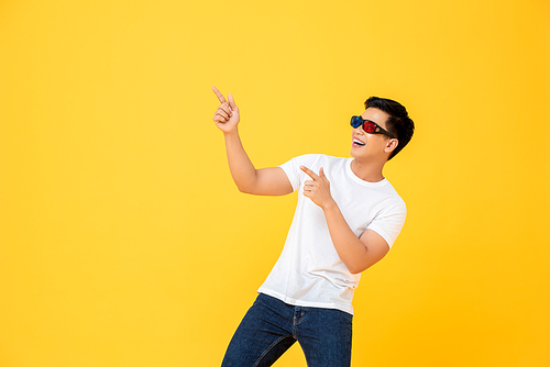 Fun Portrait of happy young Asian man wearing 3D cinema glasses pointing both fingers upward  in isolated studio yellow background