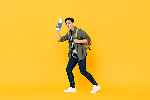 Young Asian man solo traveler with backpack passport and boarding pass ready to fly on isolated yellow background
