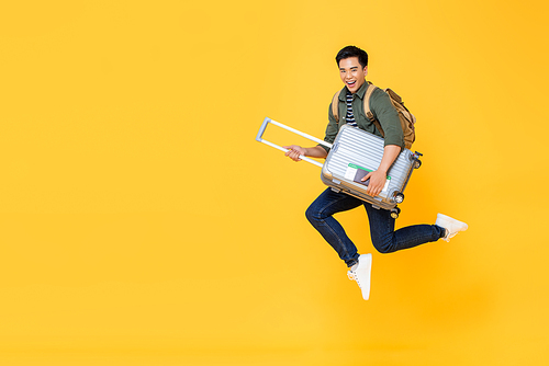 Young excited Asian tourist man with baggage jumping in mid-air ready to travel isolated on yellow background