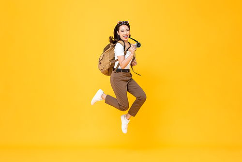 Young pretty Asian woman tourist backpacker smiling and jumping with camera in hand isolated on yellow background