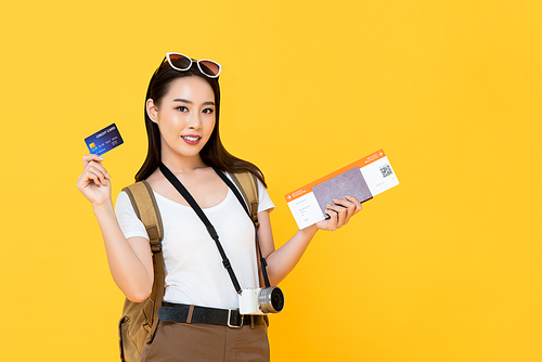 Beautiful Asian tourist woman in yellow background holding passport and boarding pass ready to travel with credit card