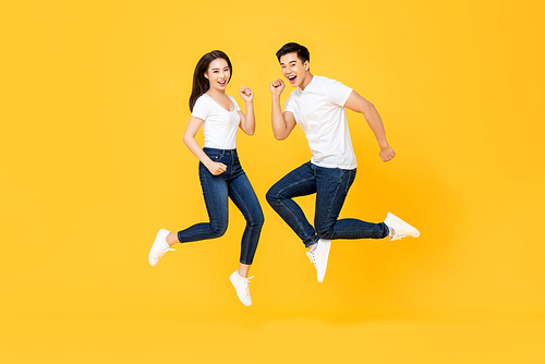 Full length portrait of lovely Asian couple smiling and jumping in mid-air isolated on yellow background