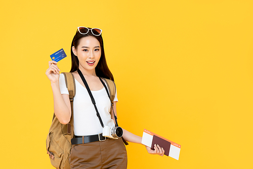 Beautiful Asian tourist woman in yellow background holding passport and boarding pass ready to travel with credit card