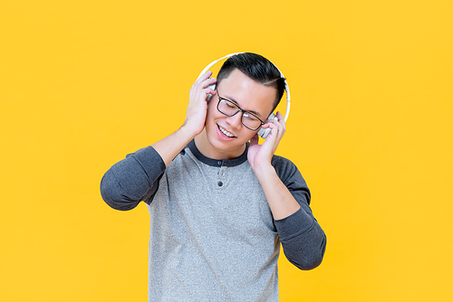 Happy Asian man wearing headphones listening to relaxing music with eyes closed isolated on yellow background