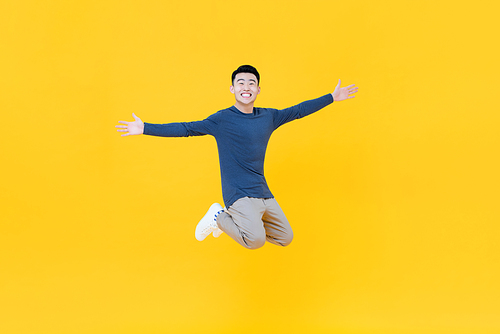 Full body of young dynamic handsome Asian man smiling and jumping with arms outstretched  isolated on yellow background
