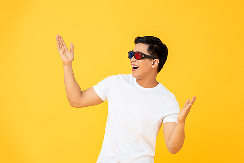 Fun Portrait of excited young Asian man wearing 3D cinema glasses with both hands raised in isolated studio yellow background