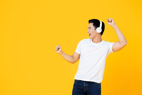 Young handsome Asian man wearing headphones listening to music and dancing on yellow background