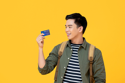 Young Asian tourist man holding credit card ready to travel isolated on yellow background