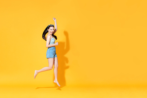 Energetic smiling beautiful Asian woman in summer outfit jumping isolated on yellow background