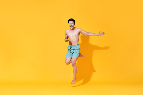 Energetic smiling shirtless handsome Asian man jumping with open hand isolated on yellow background