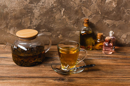 Cup of tea near teapot and blurred bottles on wooden surface on textured stone background