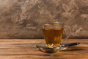 Cup of tea on saucer and spoon on wooden surface on textured stone background