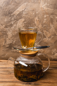 Cup of tea on glass teapot on wooden surface on textured stone background