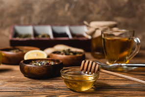 Bowl with honey near blurred tea on wooden surface on brown background