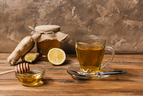 Tea and honey in bowl on wooden surface on textured stone background