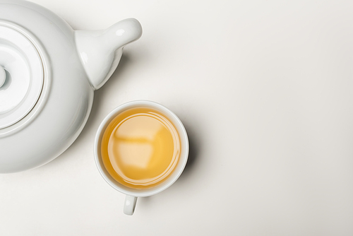 Top view of cup of tea and teapot on white background