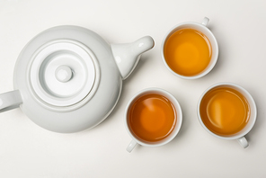Top view of cups of tea near teapot on white background
