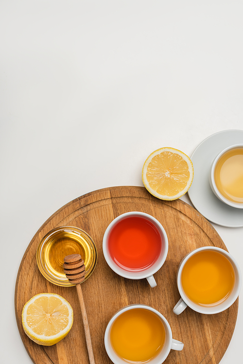 Top view of cups of tea near lemon and honey on chopping board on white background