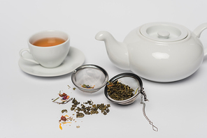 Dry tea in infuser near cup and teapot on white background