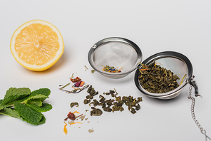 Dry tea in infuser near mint and lemon on white background