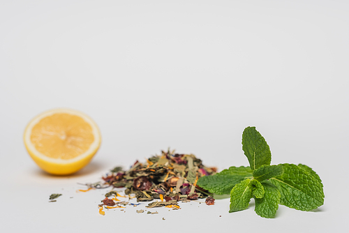 Close up view of mint near dry tea and blurred lemon on white background